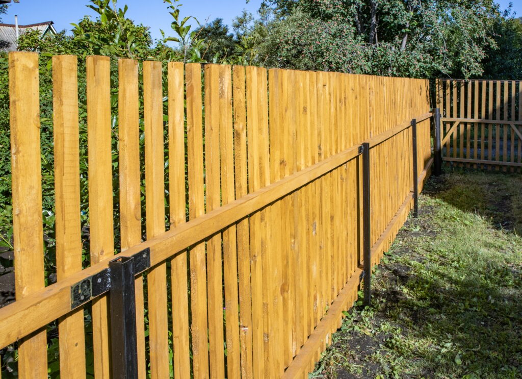 Close-up of a new wooden picket fence in the backyard of a country house, a sunny summer day