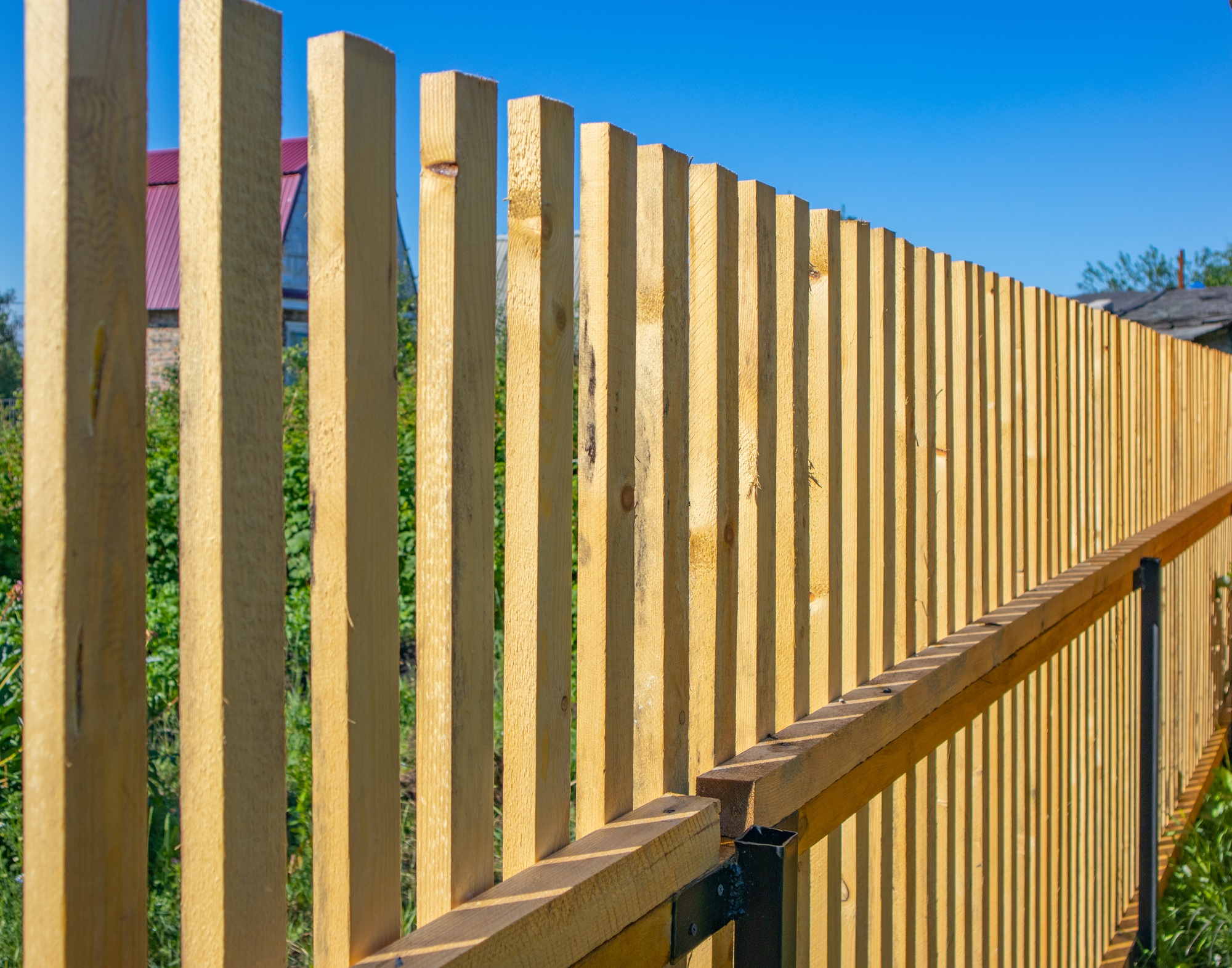 Close-up of a new wooden picket fence in the backyard of a country house, a sunny summer day